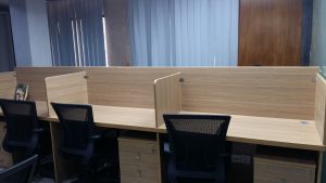Office workstation with wooden-colored particle board partitions and ergonomic chairs.