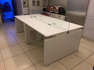 Minimalist white office workstation for four people, featuring integrated power outlets and privacy glass dividers.
