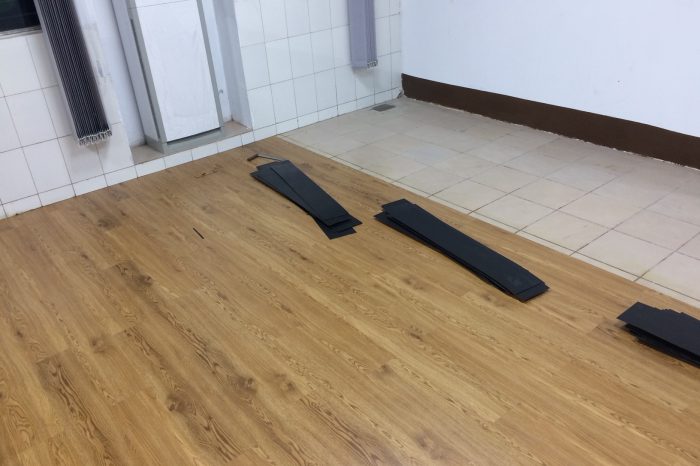 PVC floor mats being installed in a room, with partially fitted wooden-patterned tiles.