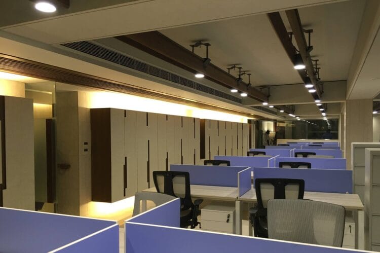 Office workstations with blue partitions, ergonomic chairs, and modern desk setup.