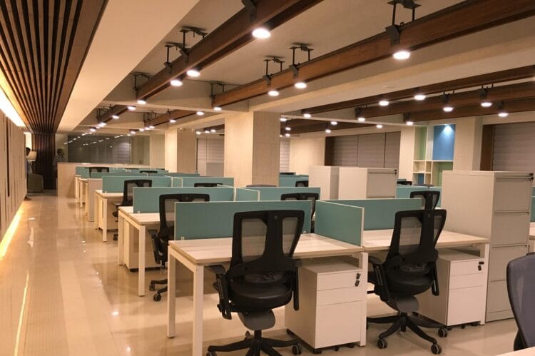 Office workstations with teal partitions, ergonomic chairs, and storage units.