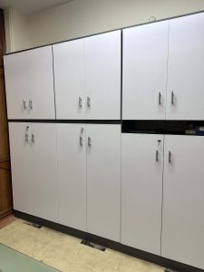 An office file cabinet with multiple compartments, featuring white doors and handles, arranged in two rows.