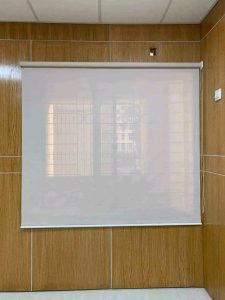 Translucent white roller blind with pull chain on warm wood-paneled office wall filtering light