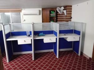 Office cubicle workstation with a single fabric partition and aluminum frame, featuring a hanging drawer unit for added storage.