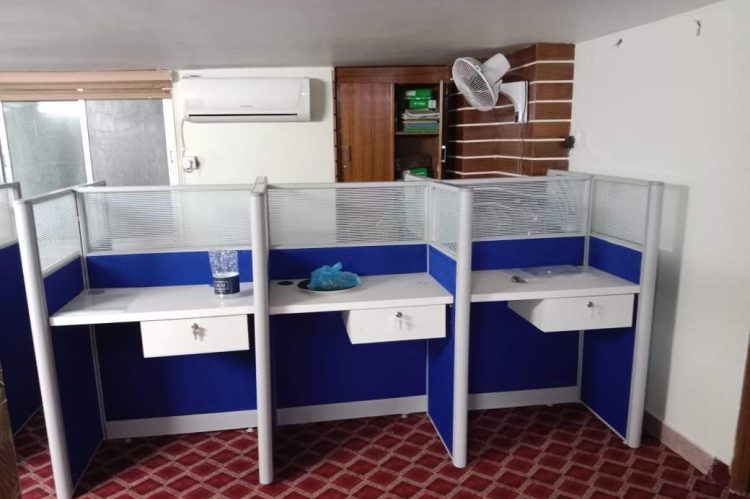 Office cubicle workstation with a single fabric partition and aluminum frame, featuring a hanging drawer unit for added storage.